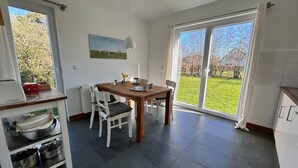 Eine moderne Küche mit Esstisch, Stühlen und Blick auf eine grüne Landschaft durch große Fenster.