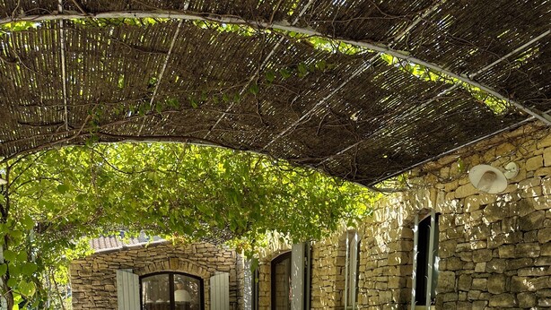 An outdoor patio with wicker furniture, stone walls, and a pergola providing shade. - Charming Mas in quiet Provence, between Luberon and Alpilles (Robion)