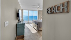 Un dormitorio con vista a la playa, un ventilador de techo y un letrero de madera que dice 'BEACH'.