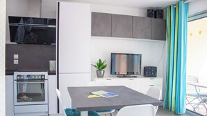 Eine moderne Küche mit Einbauofen, einem Esstisch mit Stühlen, einem Fernseher und einem Blumentopf.