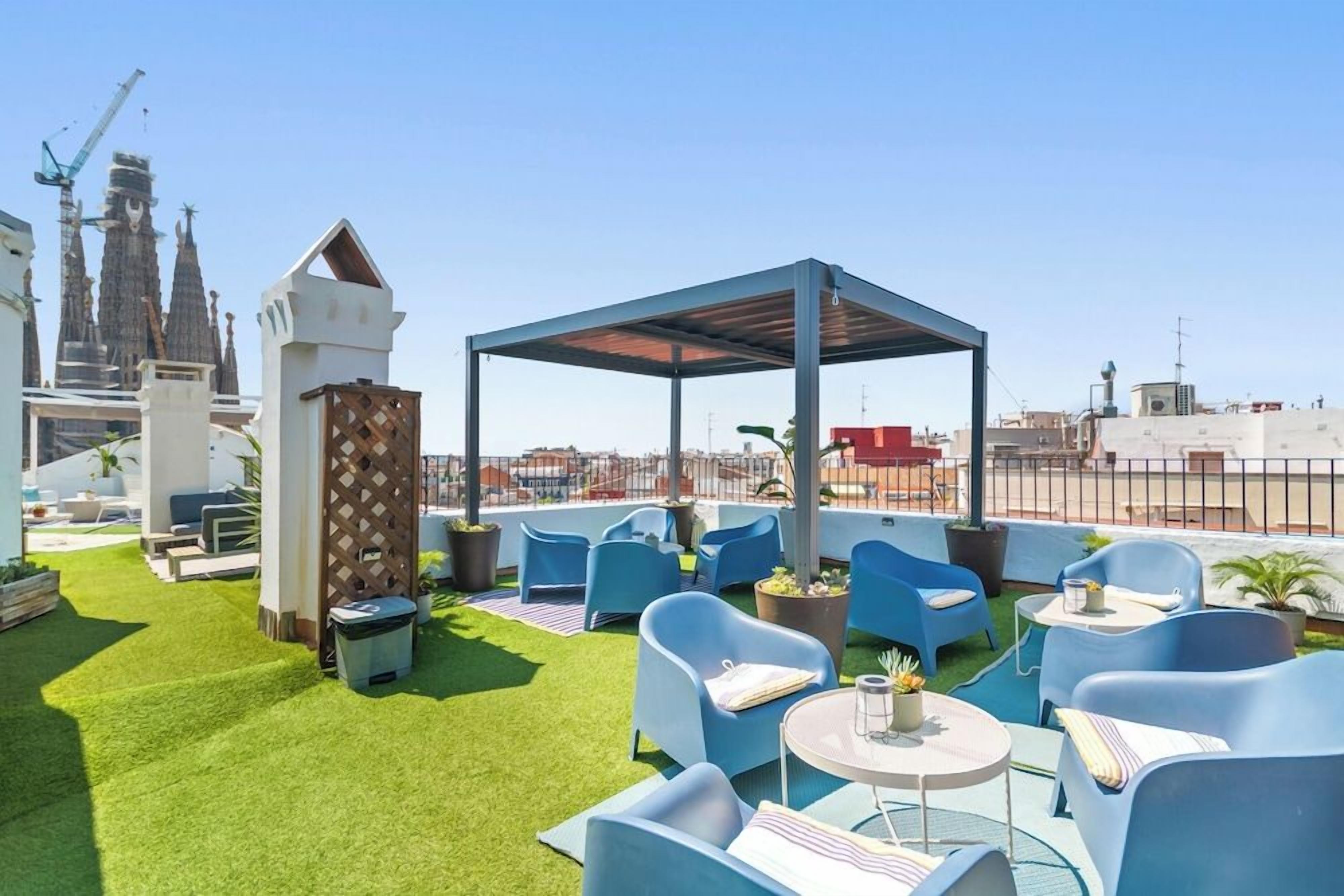 A rooftop terrace with blue chairs, a covered seating area, and a view of a cityscape with buildings and a construction crane.
