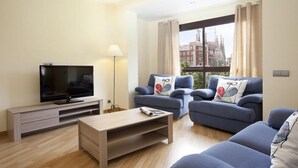 A modern living room with a flat-screen TV, two sofas with patterned cushions, a coffee table, and a lamp. - Suite Home Sagrada Familia (Barcelona)