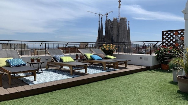 A rooftop terrace with lounge chairs and artificial grass, overlooking a construction site and a cathedral. - Suite Home Sagrada Familia (Barcelona)