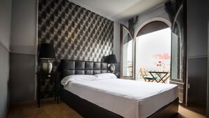 A modern hotel room with a large bed, a tufted headboard, a nightstand with a lamp, and a view of the city through a large window. - Suite Home Sagrada Familia (Barcelona)