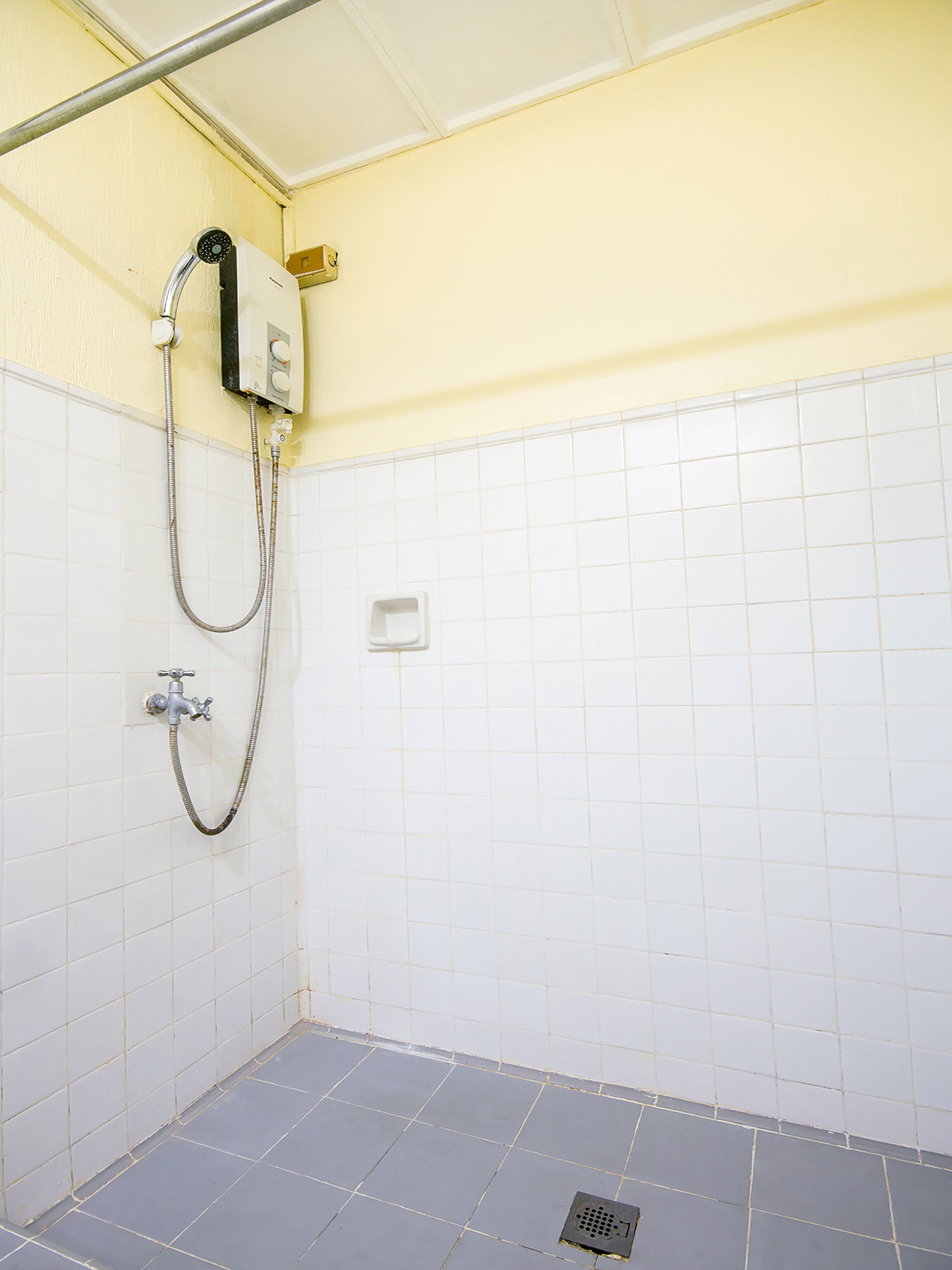 A bathroom with white tiled walls, a shower with a handheld showerhead, and a drain on the floor.