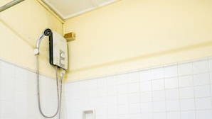 A bathroom with white tiled walls, a shower with a handheld showerhead, and a drain on the floor.