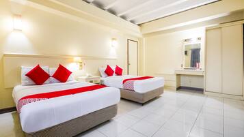 A hotel room with two beds, each with red pillows, a nightstand, a mirror, and a bathroom with a sink and mirror.