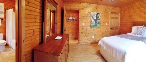 A wooden cabin room with a bed, a wooden dresser, a toilet, and a mirror.