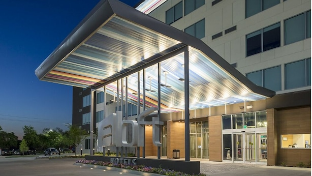 A modern hotel with a prominent 'HOTELS' sign, large windows, and a covered entrance area. - Aloft by Marriott Dallas DFW Airport Grapevine (Coppell)