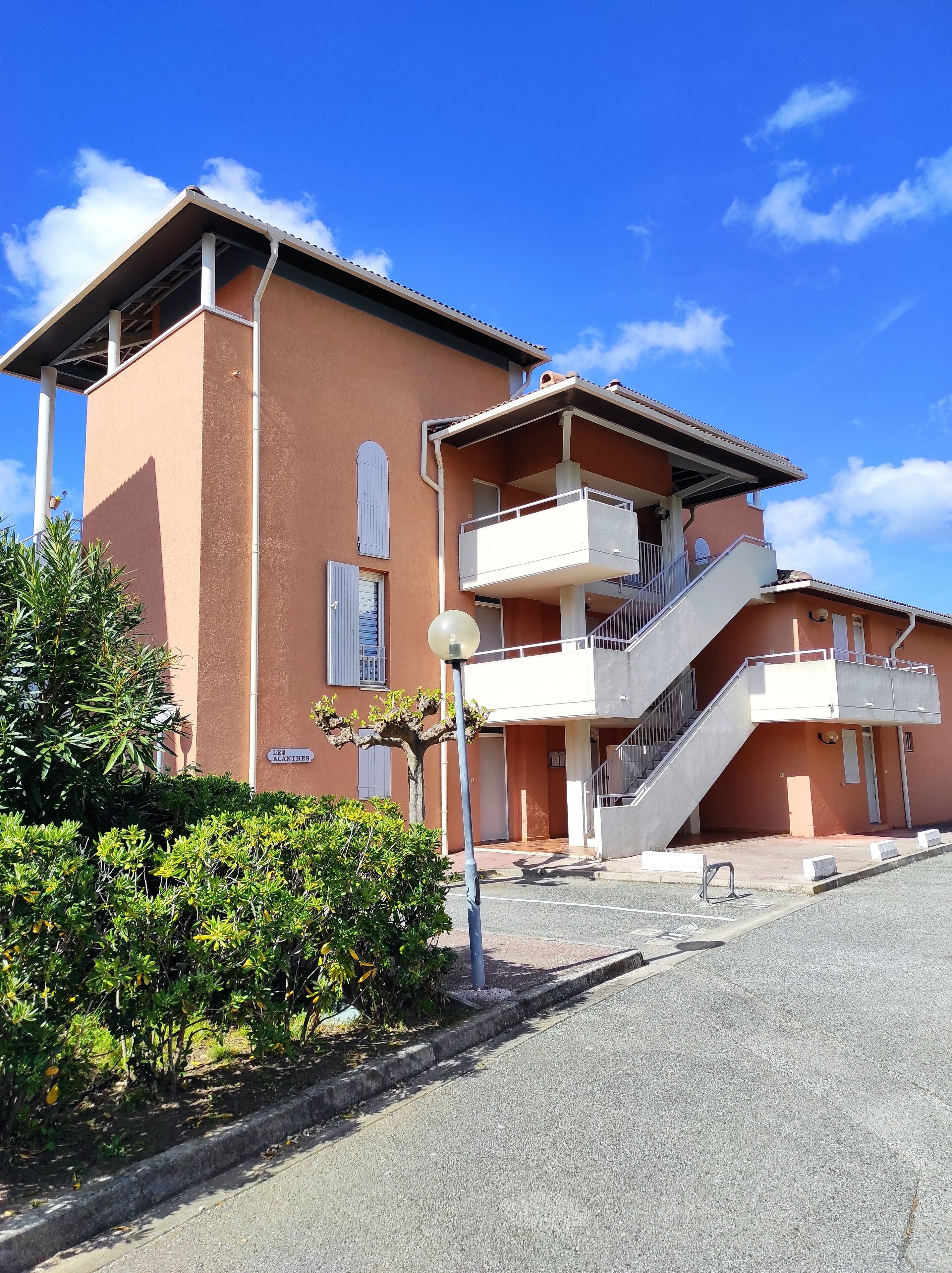 A two-story building with a balcony on the upper floor, a staircase leading to the upper level, and a sign indicating the name "LES ACANTHES".