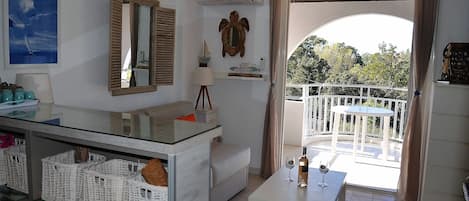 A modern living room with a balcony, a sofa, a dining table, and a kitchen area with baskets.