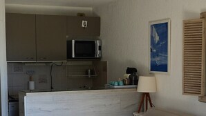 A compact living space with a kitchenette, a sofa with orange cushions, a white coffee table, and a lamp. - SEA VIEW-STUDIO 2 PERSONS- Classified 3 *- TERRASSE ABRITEE -CLIM-PARKING PRIVE (Le Lavandou)