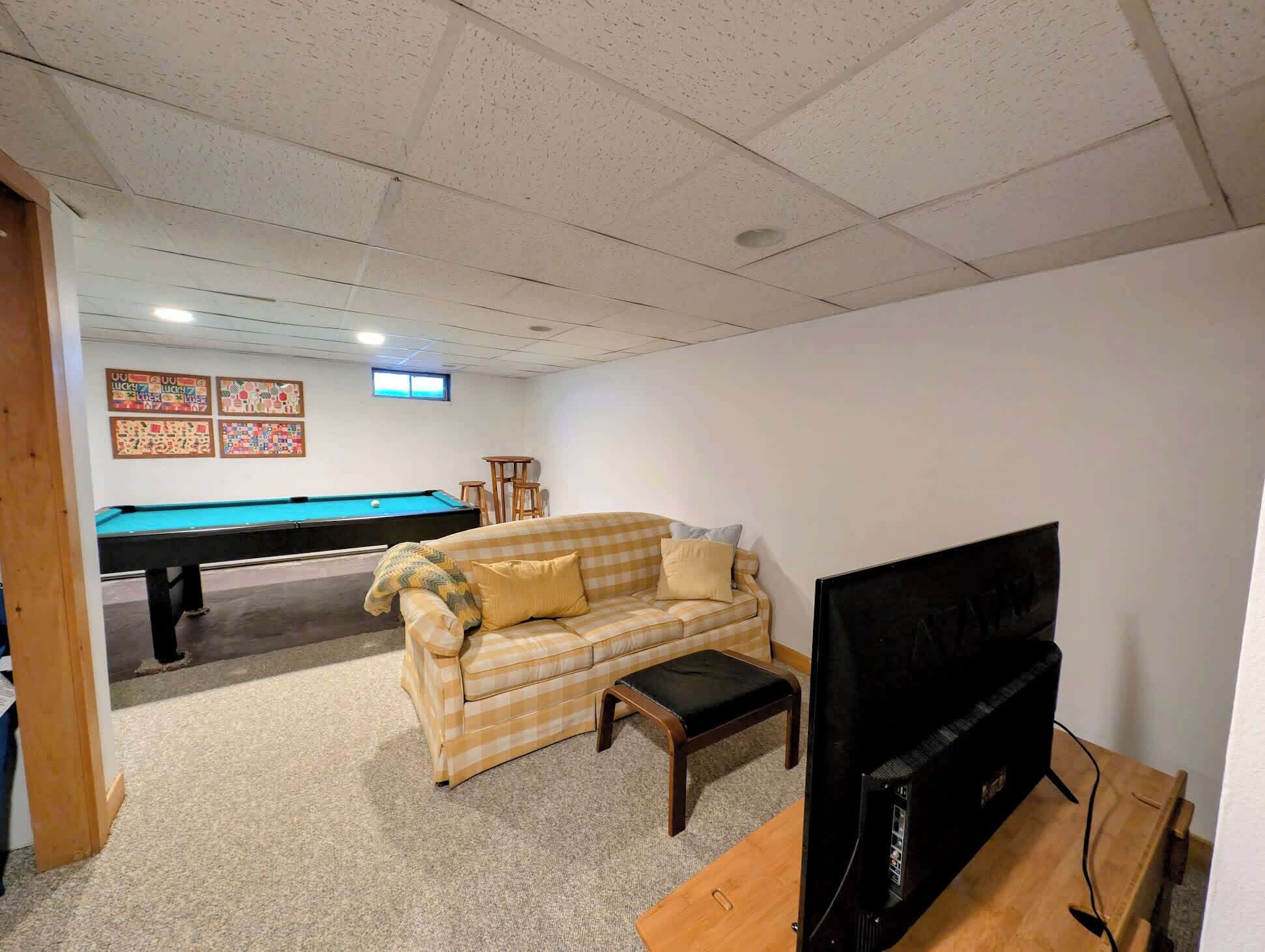 Een kamer met een pooltafel, een bank, een televisie en een plafond met inbouwverlichting.