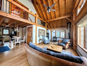 A spacious living area with a high ceiling, wooden beams, a dining area, and a cozy seating arrangement.