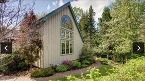Ein eingeschossiges Haus mit Satteldach, einer Veranda und einem kleinen Garten mit unterschiedlichen Pflanzen und einem Weg zum Eingang.