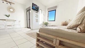Et moderne soveværelse med en seng, et tv ophængt på væggen og et spiseområde med stole og et bord.