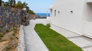 A modern outdoor area with a stone wall, a grassy lawn, and a white building. - Villa Marine, New Luxury Villa with Amazing Seaview & Private Pool (Bali)