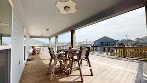 Un espace extérieur abrité, doté d’une terrasse en bois, d’une table avec des chaises et offrant une vue sur les maisons au loin.