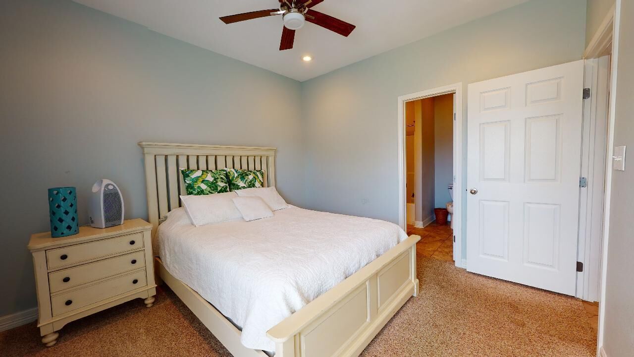 A bedroom with a bed, a nightstand, a ceiling fan, and a door.