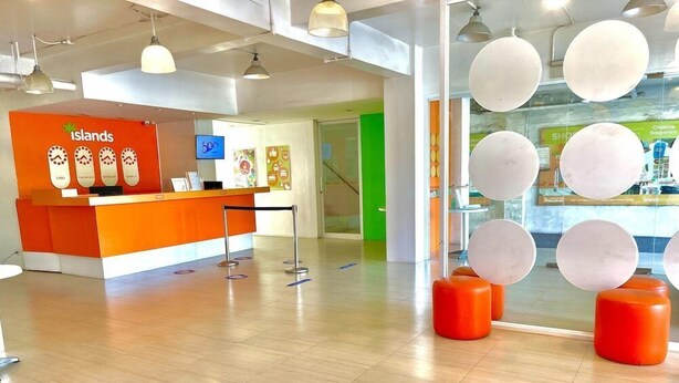 A reception area with an orange counter, a digital screen, and a green door in the background. - Islands Stay Hotel Mactan (Lapu-Lapu)