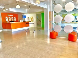 A reception area with an orange counter, a digital screen, and a green door in the background. - Islands Stay Hotel Mactan (Lapu-Lapu)
