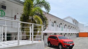 A red SUV parked in front of a building with a white facade and a green sign with the number 11. - Islands Stay Hotel Mactan (Lapu-Lapu)