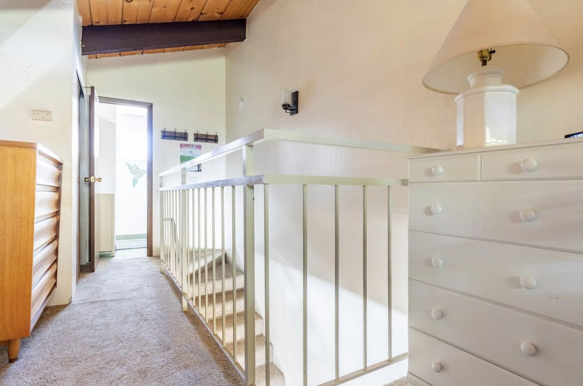 A hallway with a staircase, a white dresser, and a lamp.