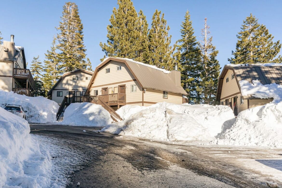 A snow-covered road leading to a cabin-style building with a wooden deck and a chimney.