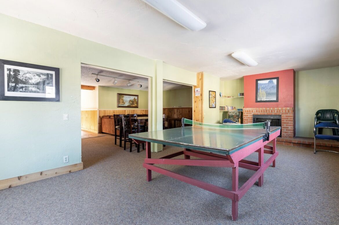 A room with a ping pong table, chairs, a fireplace, and framed pictures on the walls.