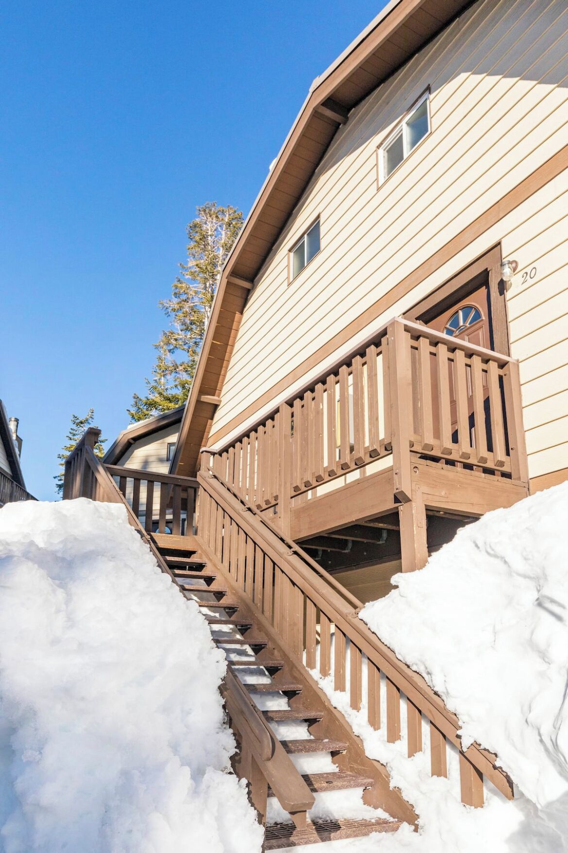 A wooden staircase leading to a house with a balcony, surrounded by snow.