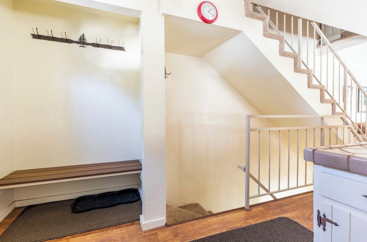Un escalier avec une rampe en bois et un mur blanc orné d’une horloge.