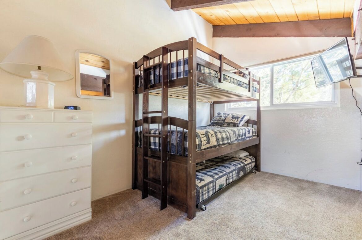Cama litera con espejo y cómoda en una habitación con ventana.