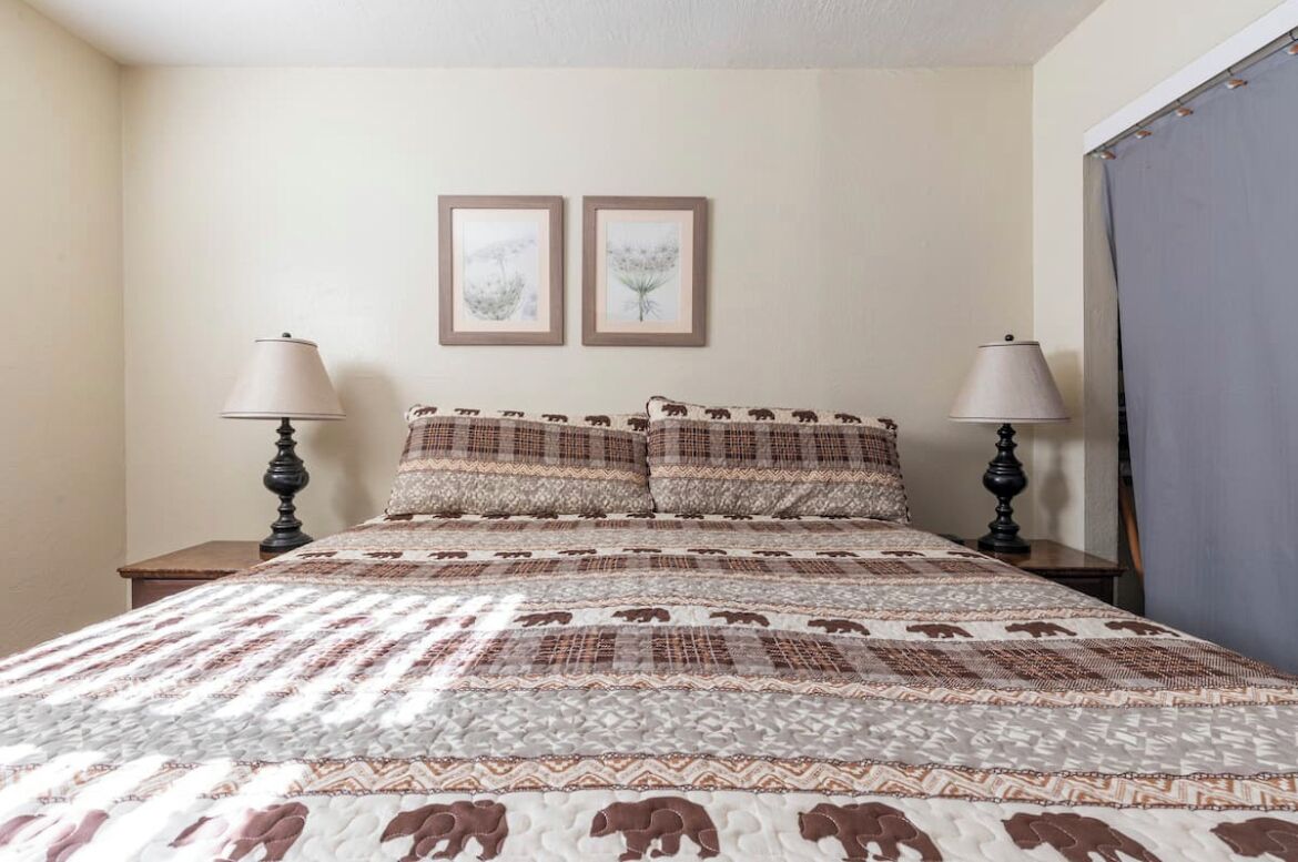 A bed with a patterned bedspread and two matching pillows, flanked by two nightstands with lamps.