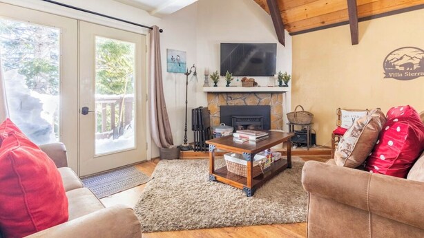 A cozy living room with a fireplace, a television mounted above it, and a stone wall. - Mammoth View Villas 20-Nice townhome close to the Village (Mammoth Lakes)