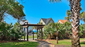 A pathway leading to a covered gazebo in a well-maintained garden with palm trees and a house in the background. - Balcony Views of the Gulf, Zero-Entry Pool, Free Beach Chair Service (Miramar Beach)