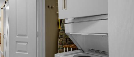 A laundry room with a front-loading washer and dryer, a door, and a wall with a poster.