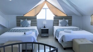 A modern, well-lit attic bedroom with two beds, a small table, and a window with a view. - Grand Blue Beach Hotel (Boracay Island)