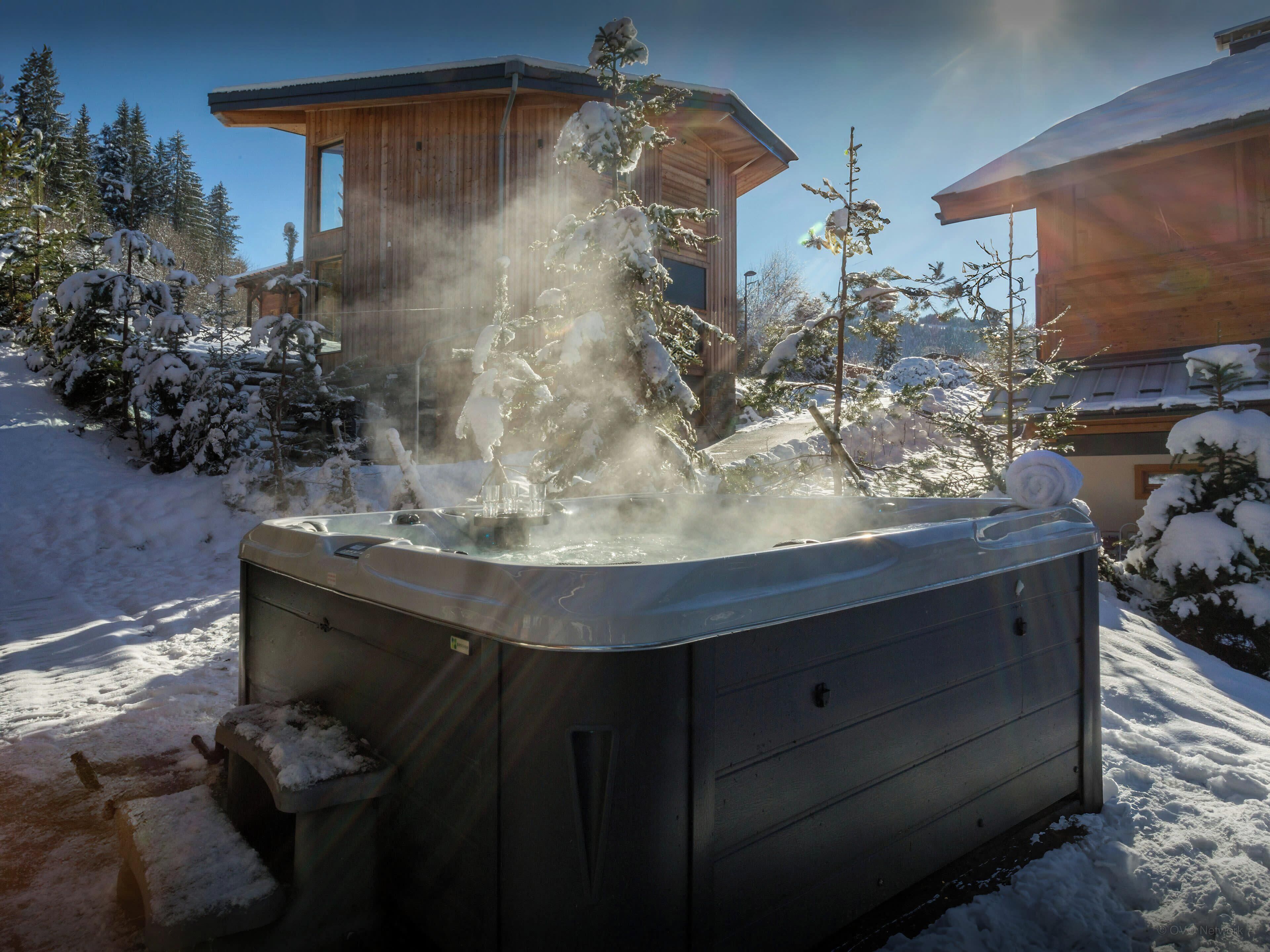 A hot tub in a snowy outdoor area with a wooden building in the background.