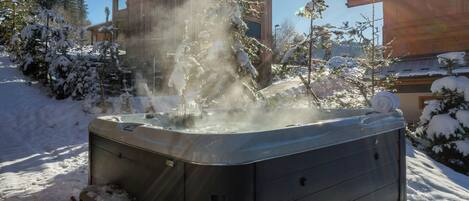 A hot tub in a snowy outdoor area with a wooden building in the background.