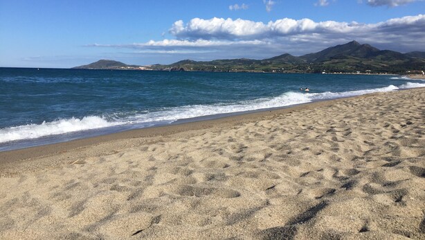 Een zandstrand met zachte golven, een heldere lucht en verre bergen.