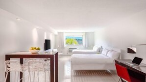Une chambre d’hôtel comprenant un lit, un bureau avec un ordinateur portable, un coin repas avec des chaises, une télévision et une fenêtre donnant sur la mer.