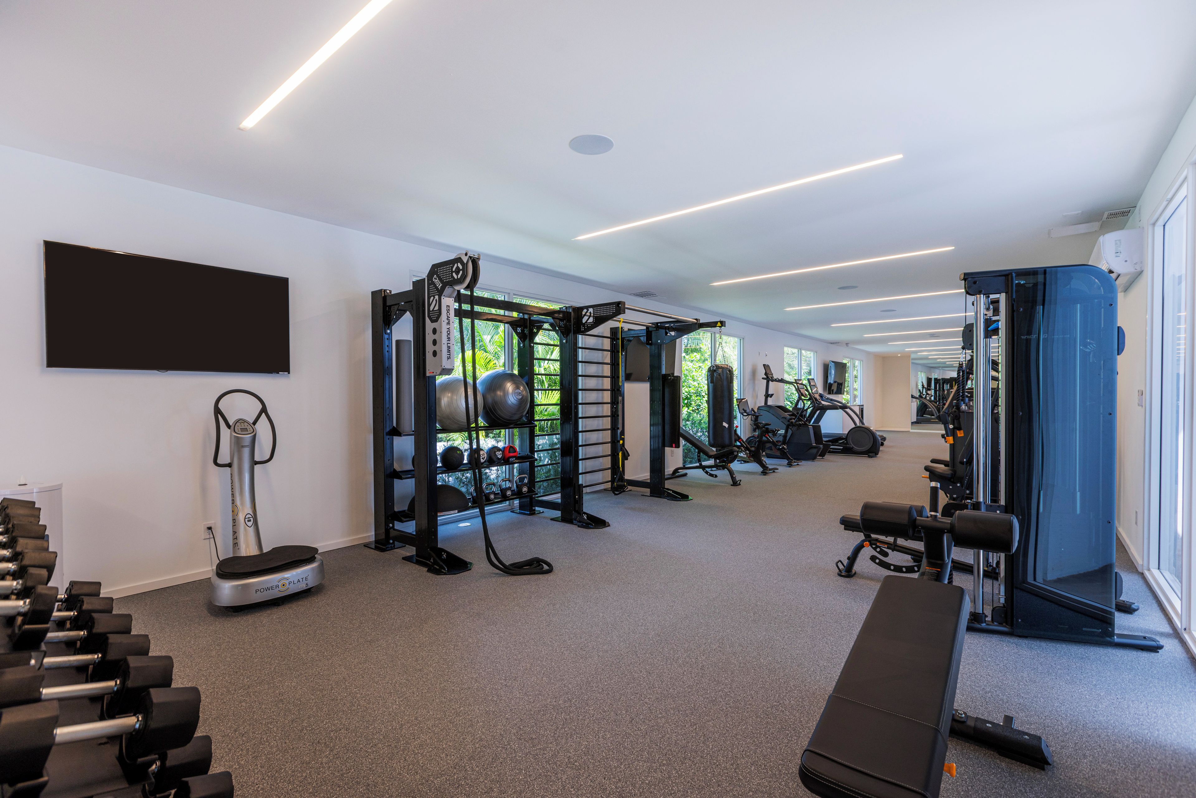 Un gimnasio con equipo de ejercicio, una banca y un televisor en la pared.