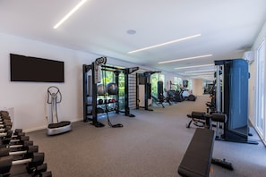 Uma academia com equipamentos de exercícios, um banco e uma televisão na parede.