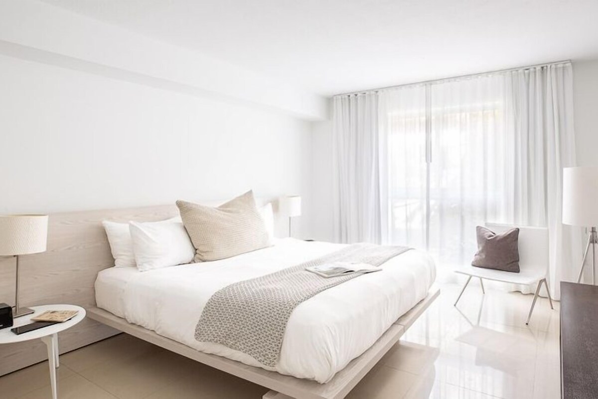 A modern hotel room with a large bed, bedside tables, a desk, and a chair.