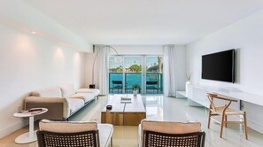 A modern living room with a sofa, coffee table, and chairs. A TV is mounted on the wall, and there is a view of the sea through large windows. - Beach Haus Bal Harbour (Bal Harbour)