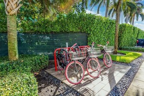 A bicycle with a basket parked on a paved area with a green hedge and palm trees in the background. - Beach Haus Bal Harbour (Bal Harbour)