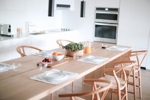 A modern kitchen with a wooden dining table set for four, equipped with chairs, plates, cutlery, and a bowl of fruit.