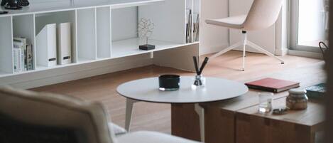 A modern living room with a flat-screen TV, a white sofa, a round coffee table, and a bookshelf.