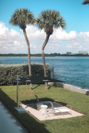 A patio area with two palm trees, a water body, and outdoor furniture. - Beach Haus Bal Harbour (Bal Harbour)
