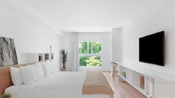 Quarto moderno com uma cama grande, uma TV na parede e uma janela com vista para o verde.
